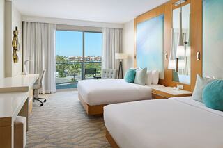 A modern hotel room features a plush bed, lounge chair, and a balcony with ocean views, exuding a serene and inviting atmosphere.