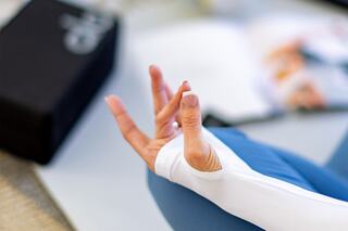 A hand in a yoga mudra gesture, resting on a mat, embodies tranquility and mindfulness. Nearby, materials suggest a focus on wellness.