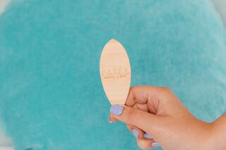 A hand holds a wooden tag marked "Patea Hotel & Spa" in front of a plush, turquoise cushion. Soft colors create a relaxing atmosphere.